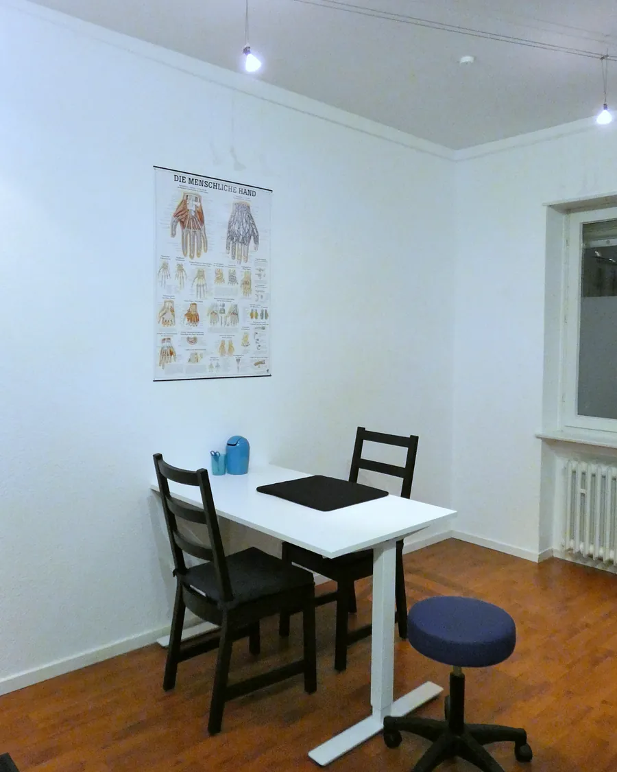 Behandlungsplatz mit Tisch, zwei Stühlen und einem Rollhocker