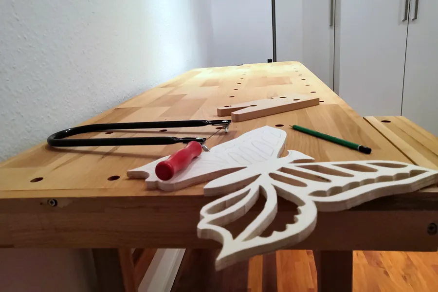 Holzwerkbank in der Praxis mit Laubsäge und einem ausgesägten Holz-Schmetterling